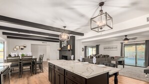 Une cuisine spacieuse dotée d’un grand îlot central, de meubles de couleur sombre et d’un lustre moderne.