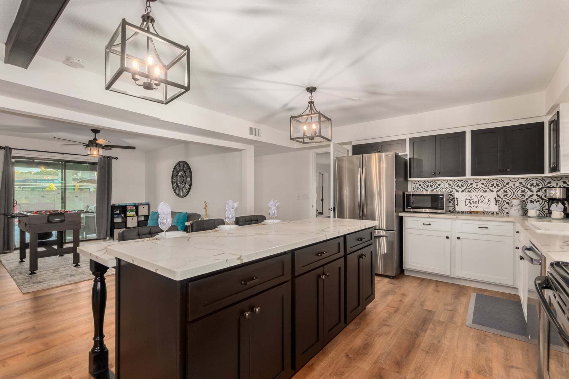 A modern kitchen with a large island, dark cabinetry, stainless steel appliances, and pendant lighting.
