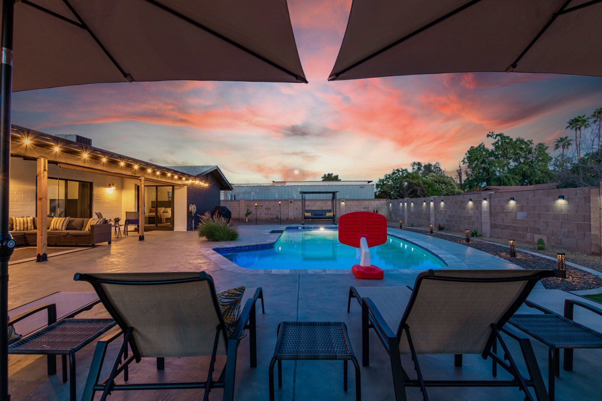 A pool area with lounge chairs, a red floating pool table, and a sunset view.