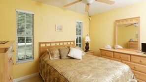 A bedroom with a bed, a nightstand, a dresser, a mirror, and a ceiling fan.
