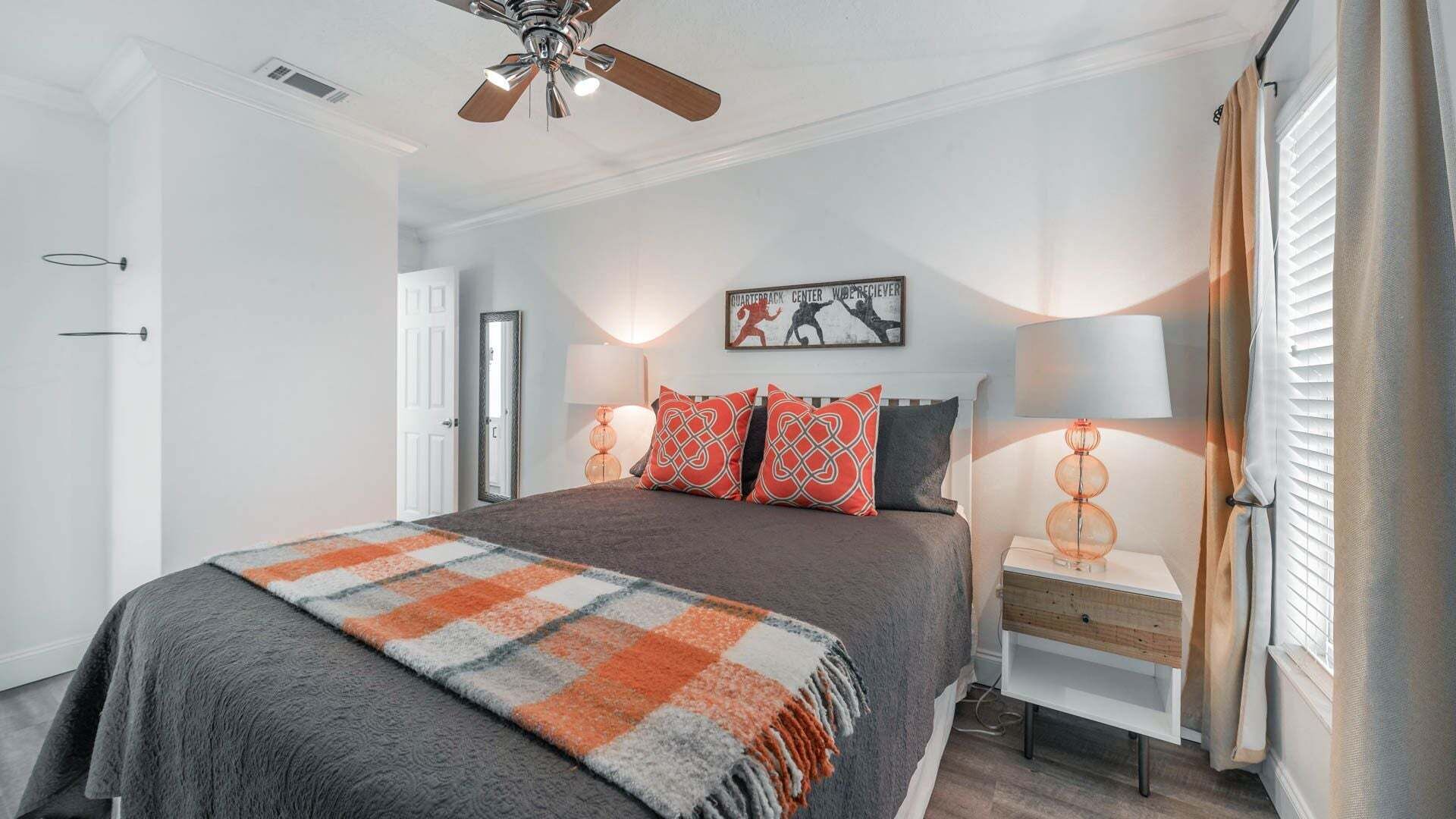 A bedroom with a bed, a ceiling fan, a nightstand, a lamp, and a door.