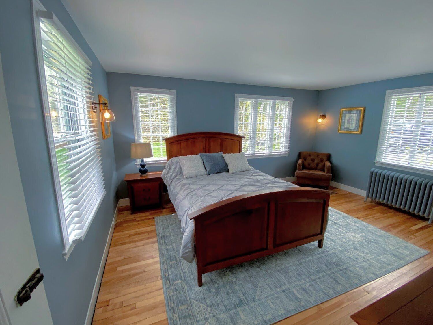 A bedroom with a wooden bed, a nightstand, a chair, and a radiator.