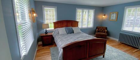 A bedroom with a wooden bed, a nightstand, a chair, and a radiator.