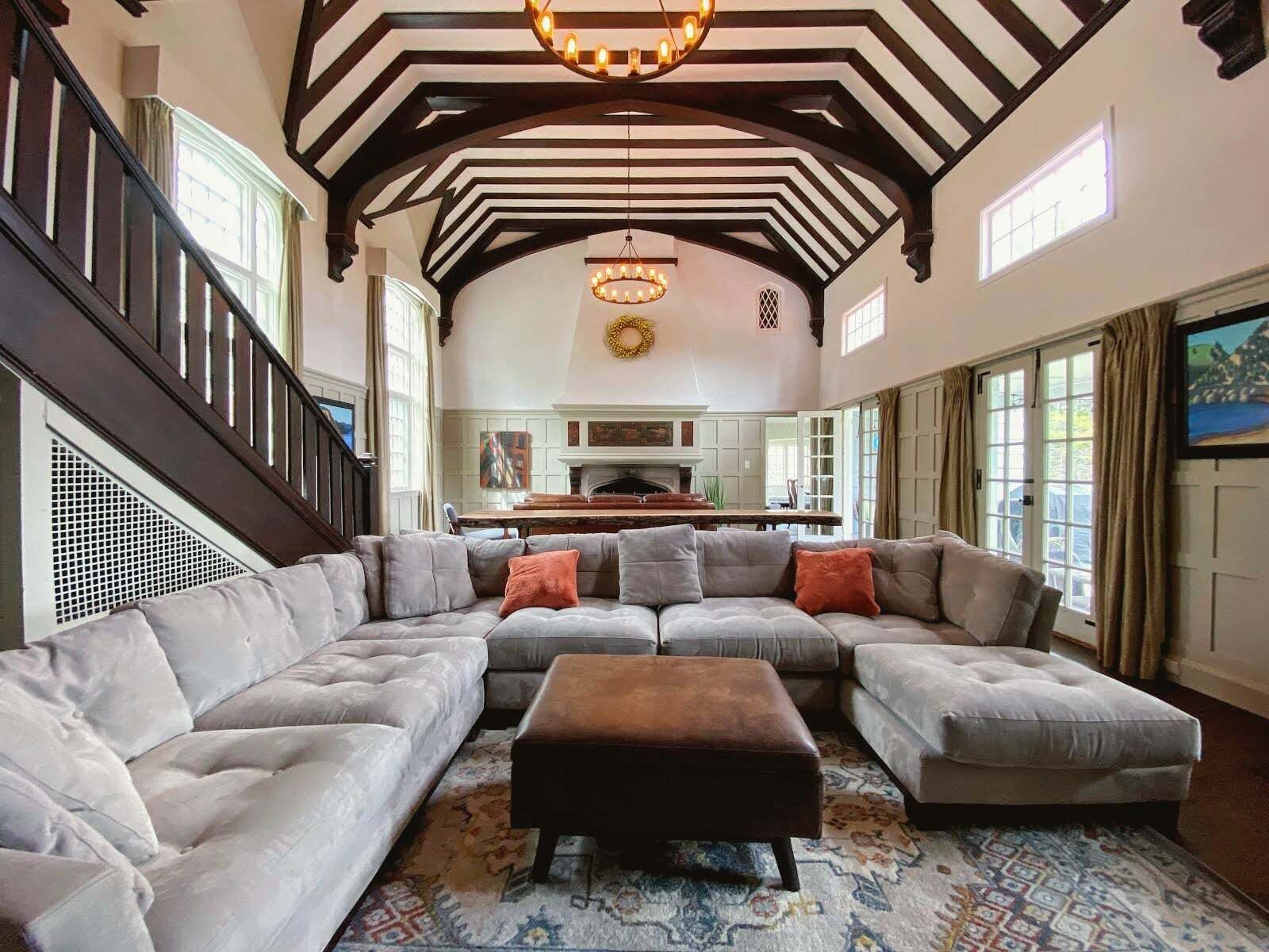 A spacious living room with a large sectional sofa, a fireplace, and a high ceiling with exposed beams.