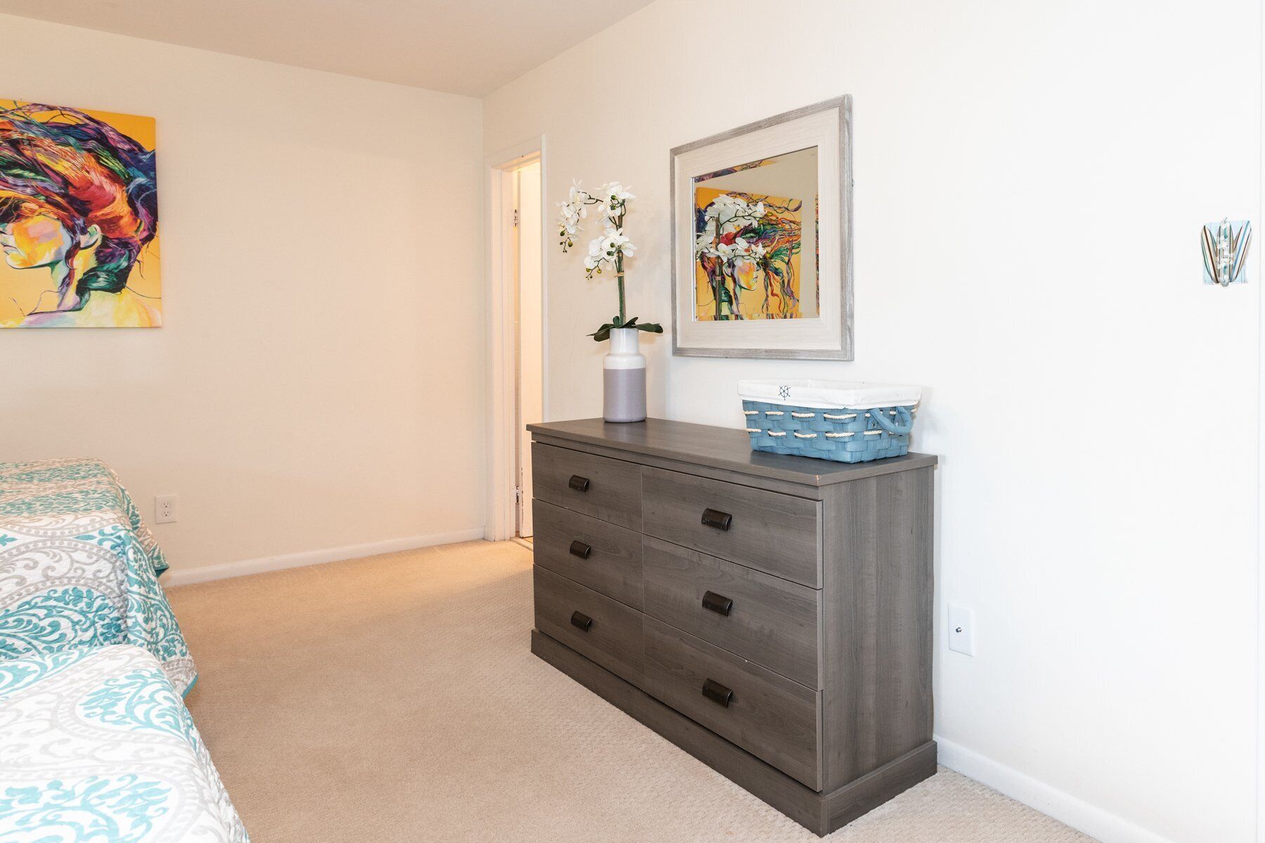 Een slaapkamer met een bed, een kaptafel, een deur en twee schilderijen aan de muur.