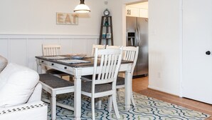 A dining area with a wooden table and white chairs, a clock, and a refrigerator in the background. - Latitude Adjustment (Virginia Beach)
