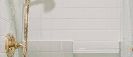 Une douche dotée d’un pommeau et d’un flexible dorés, de murs recouverts de carreaux blancs et d’un design d’angle.