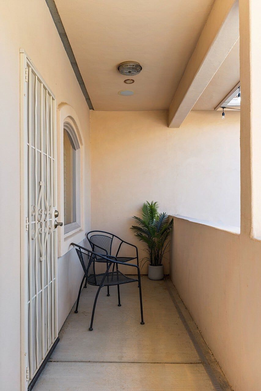 A narrow corridor with a metal gate, a potted plant, and two metal chairs.