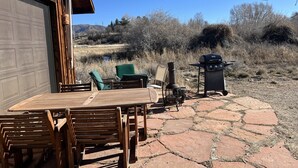 Une terrasse extérieure avec une table et des chaises en bois, un barbecue et une poubelle.