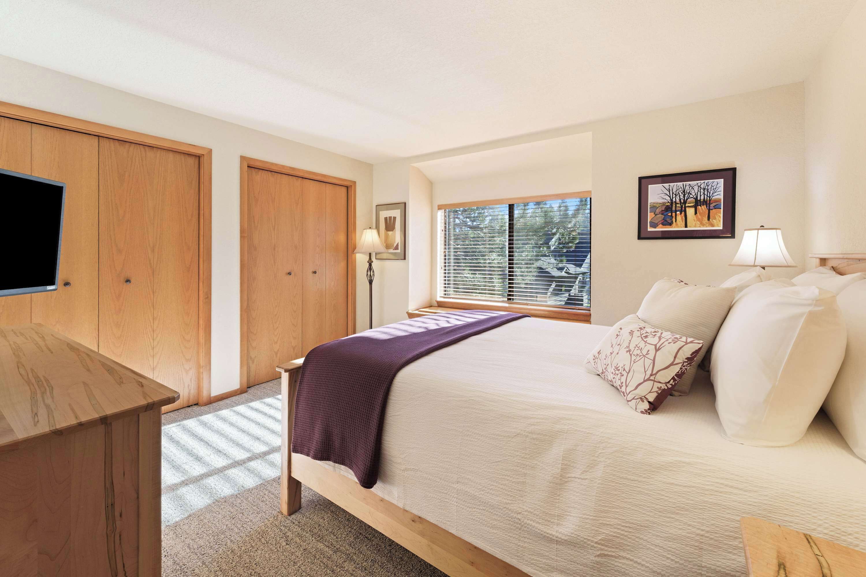 Un dormitorio con cama, escritorio, ventana con persianas y puerta.