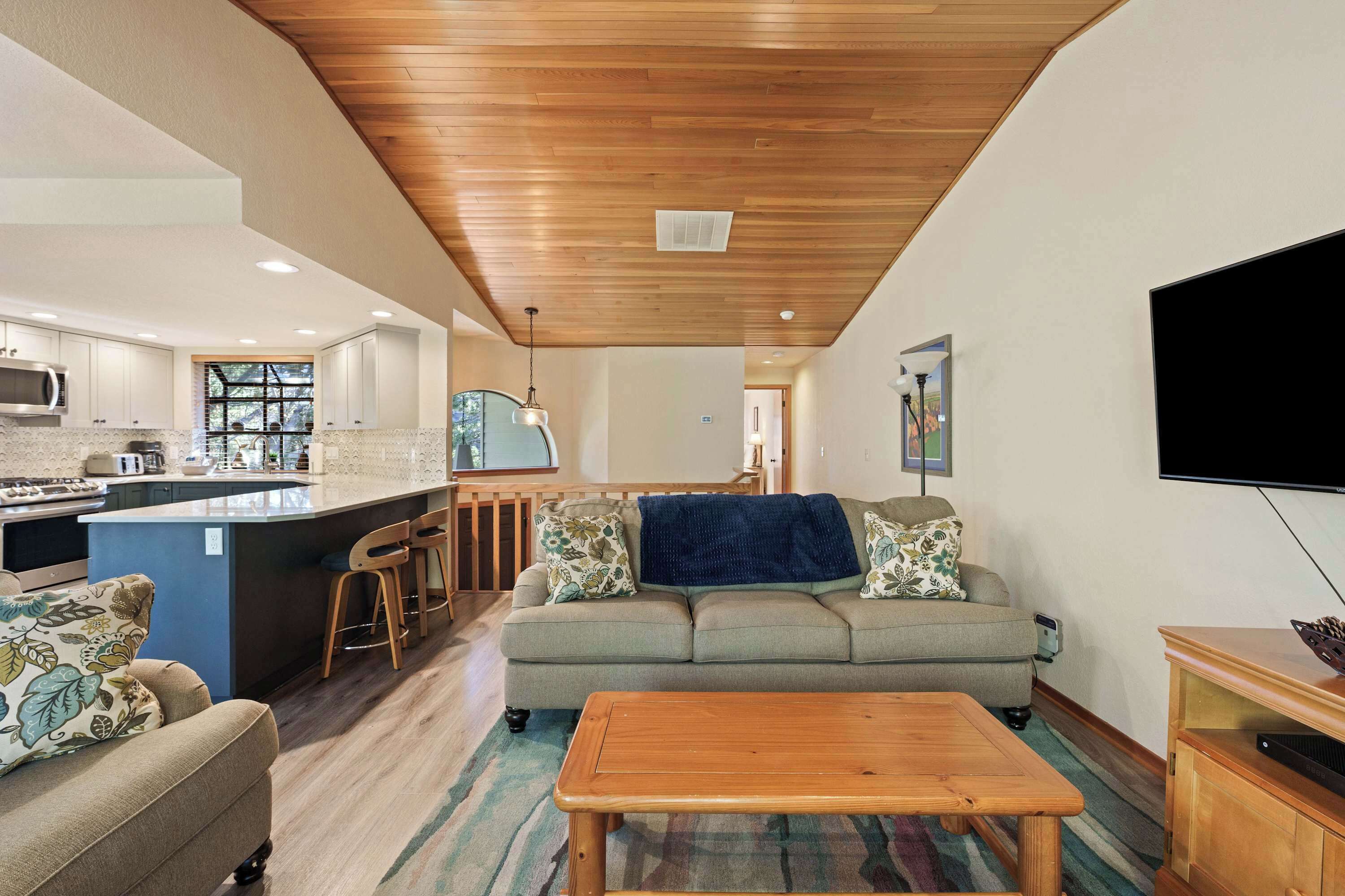 Una sala de estar moderna con techo de madera, un sofá, una mesa de centro y un televisor en la pared.