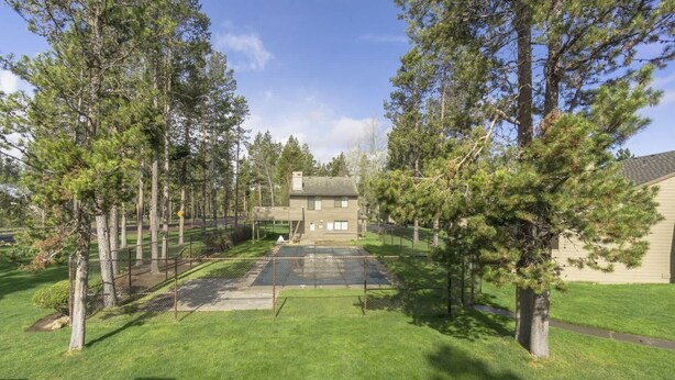 A fenced backyard with a tennis court, surrounded by tall trees and a house. - Fairway Village 8 (Bend)