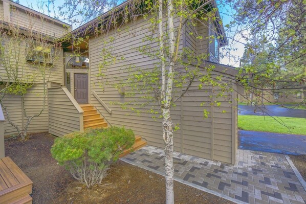 A residential house with a front porch, a small staircase, and a garden area with a tree and shrubs. - Fairway Village 8 (Bend)