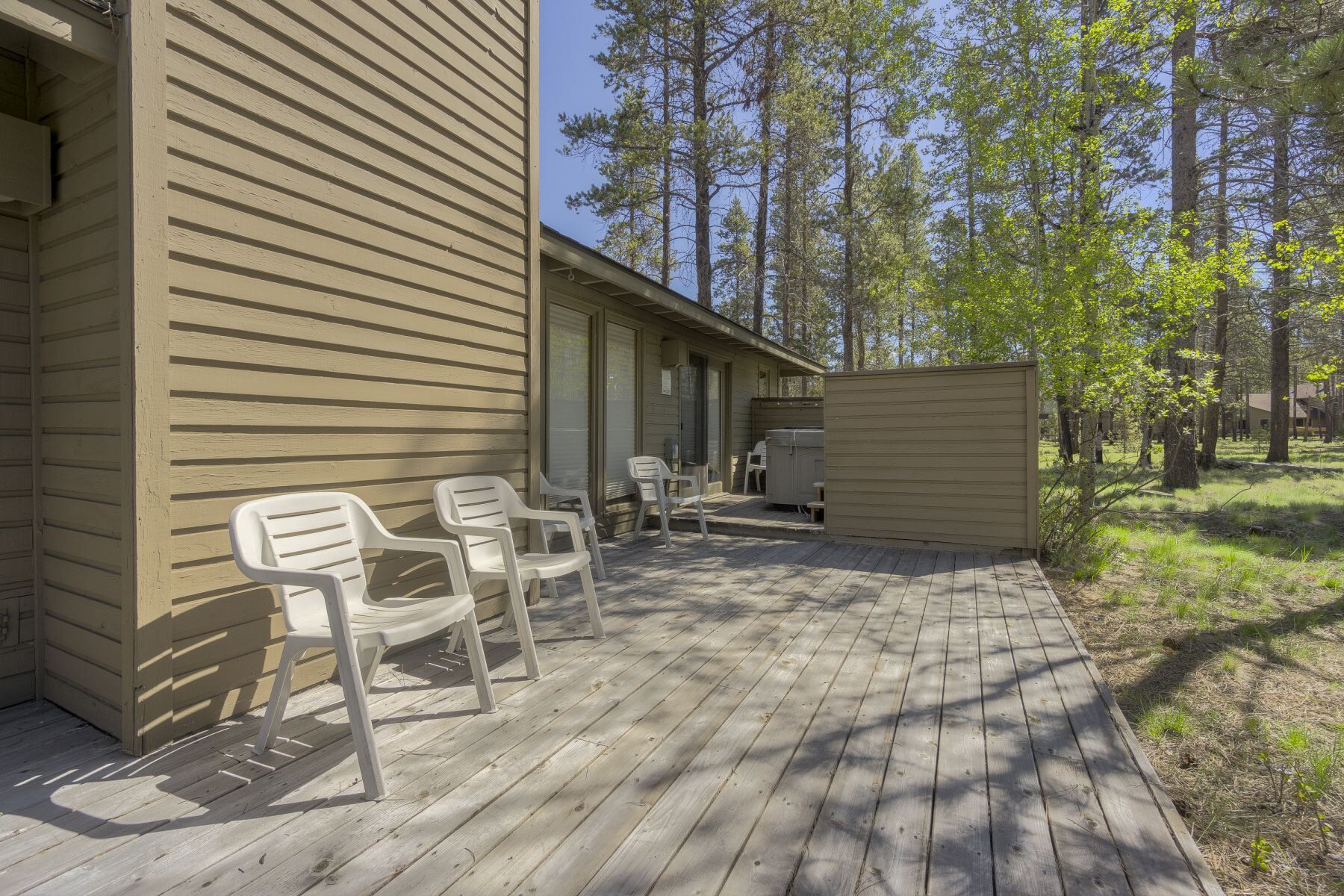 A wooden deck with plastic chairs, a hot tub, and a covered area, surrounded by trees.
