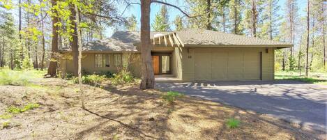 A single-story house with a garage, surrounded by a forested area.
