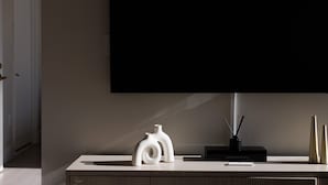 A modern living room with a flat-screen TV mounted on the wall, a minimalist white console table, and two decorative vases. - Exclusive Midtown Luxury Step From Times Square! (New York)