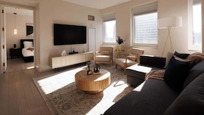 A modern living room with a flat-screen TV, a round wooden coffee table, a sofa, and a lamp. - Exclusive Midtown Luxury Step From Times Square! (New York)