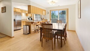 Une cuisine moderne avec des meubles en bois, un réfrigérateur en acier inoxydable et un coin repas comprenant une table et des chaises en bois.