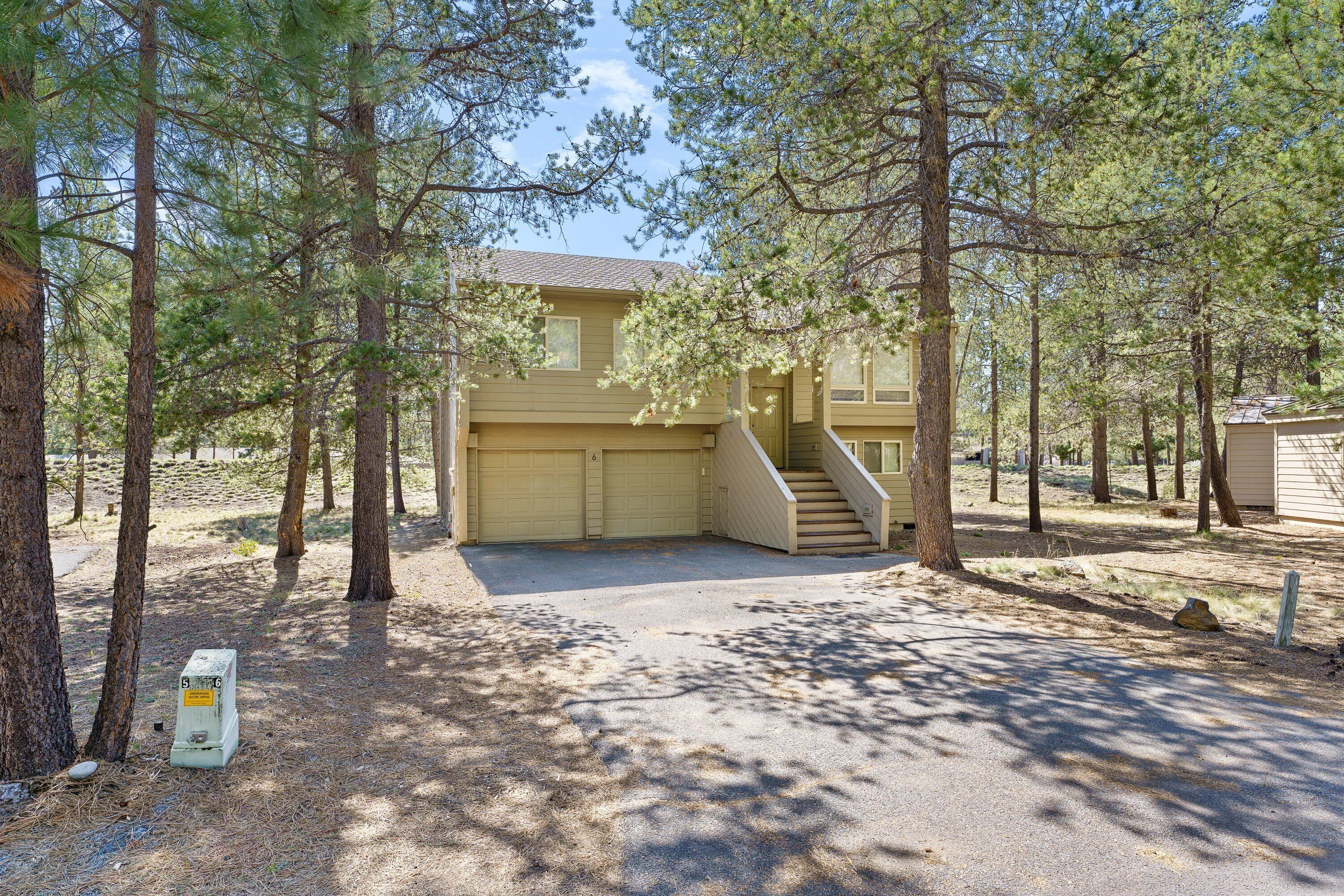 A two-story house with a garage, surrounded by tall pine trees.