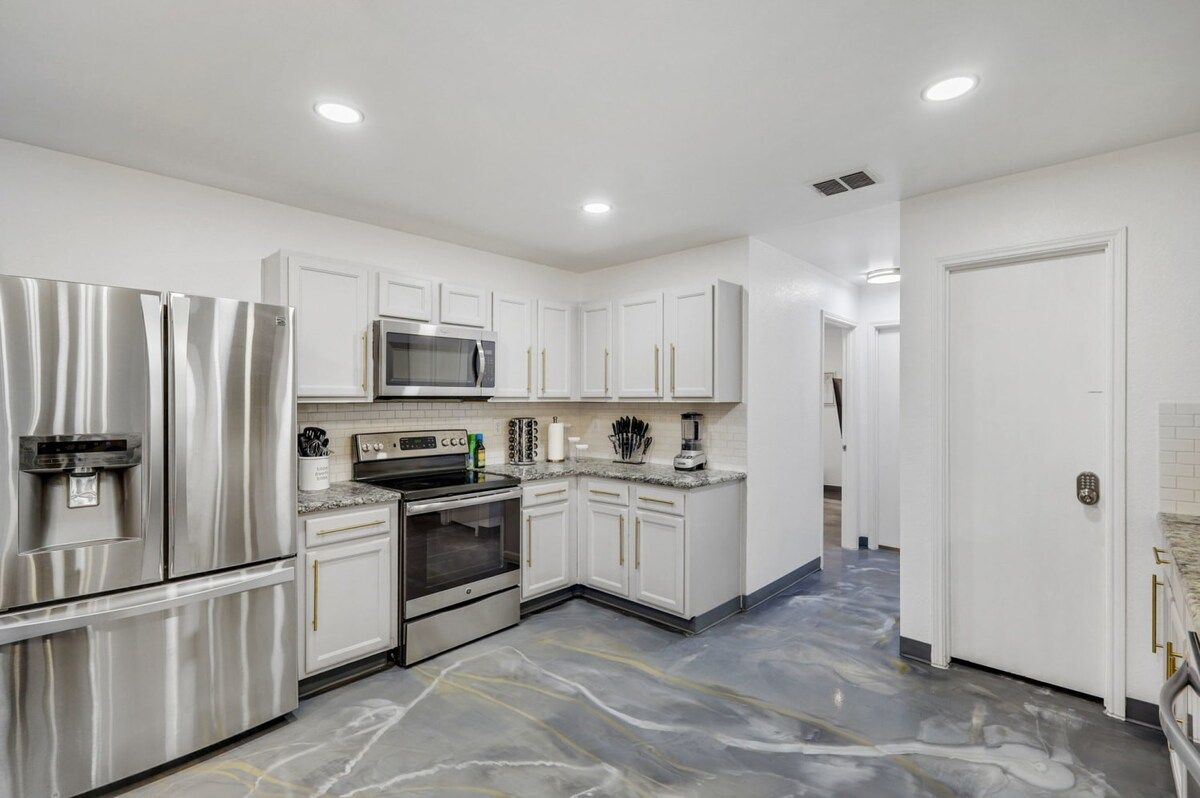 A modern kitchen with stainless steel appliances, white cabinetry, and a marble floor.