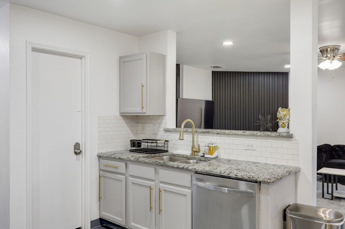 A modern kitchen with white cabinetry, a granite countertop, a stainless steel sink, and a black refrigerator.