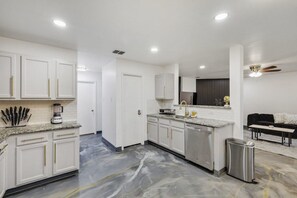 Eine moderne Küche mit weißen Schränken, Granit-Arbeitsplatten, einem Edelstahl-Geschirrspüler und einem Marmorboden.