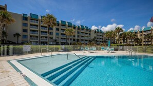 A swimming pool with clear blue water, surrounded by a white fence and palm trees. - Errol By The Sea 406 (New Smyrna Beach)