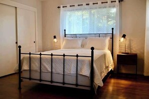 A neatly made bed with a metal frame, two bedside lamps, and a window with sheer curtains. - Lillys Maison 3 (Houston)