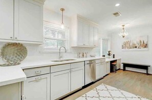 A modern kitchen with white cabinetry, a central island, and pendant lighting. - Lillys Maison 3 (Houston)
