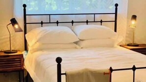 Un lit bien fait, avec des draps blancs, une structure en métal noir et une serviette rouge et blanche posée sur le pied du lit.