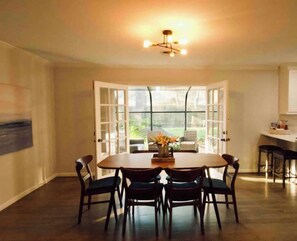 A dining area with a round table and chairs, a chandelier, and a view through open French doors. - Lillys Maison 3 (Houston)