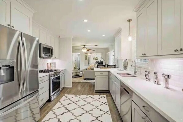 A modern kitchen with stainless steel appliances, white cabinetry, and a patterned rug. - Lillys Maison 3 (Houston)