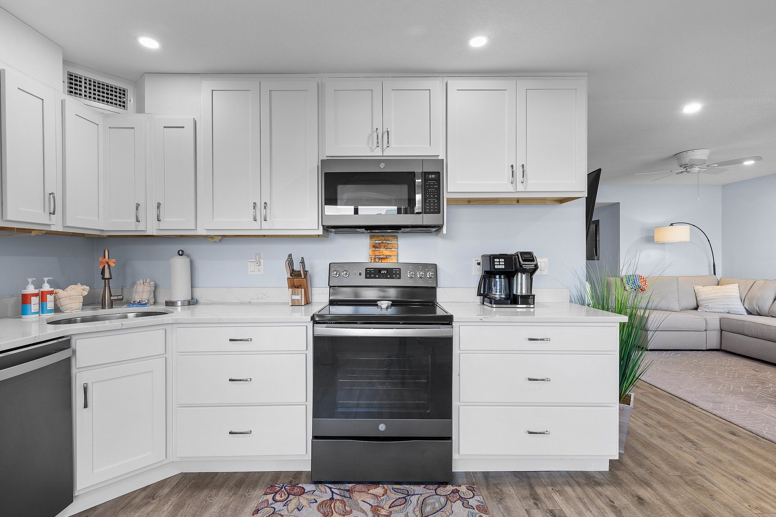 Una cocina moderna con armarios blancos, microondas integrado, estufa y cafetera.