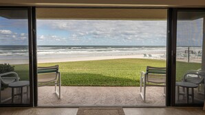 Une vue depuis un balcon donnant sur une plage, avec deux chaises et une petite table.