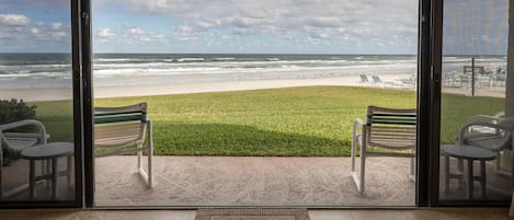 Vista desde un balcón con vista a una playa, con dos sillas y una mesa pequeña.