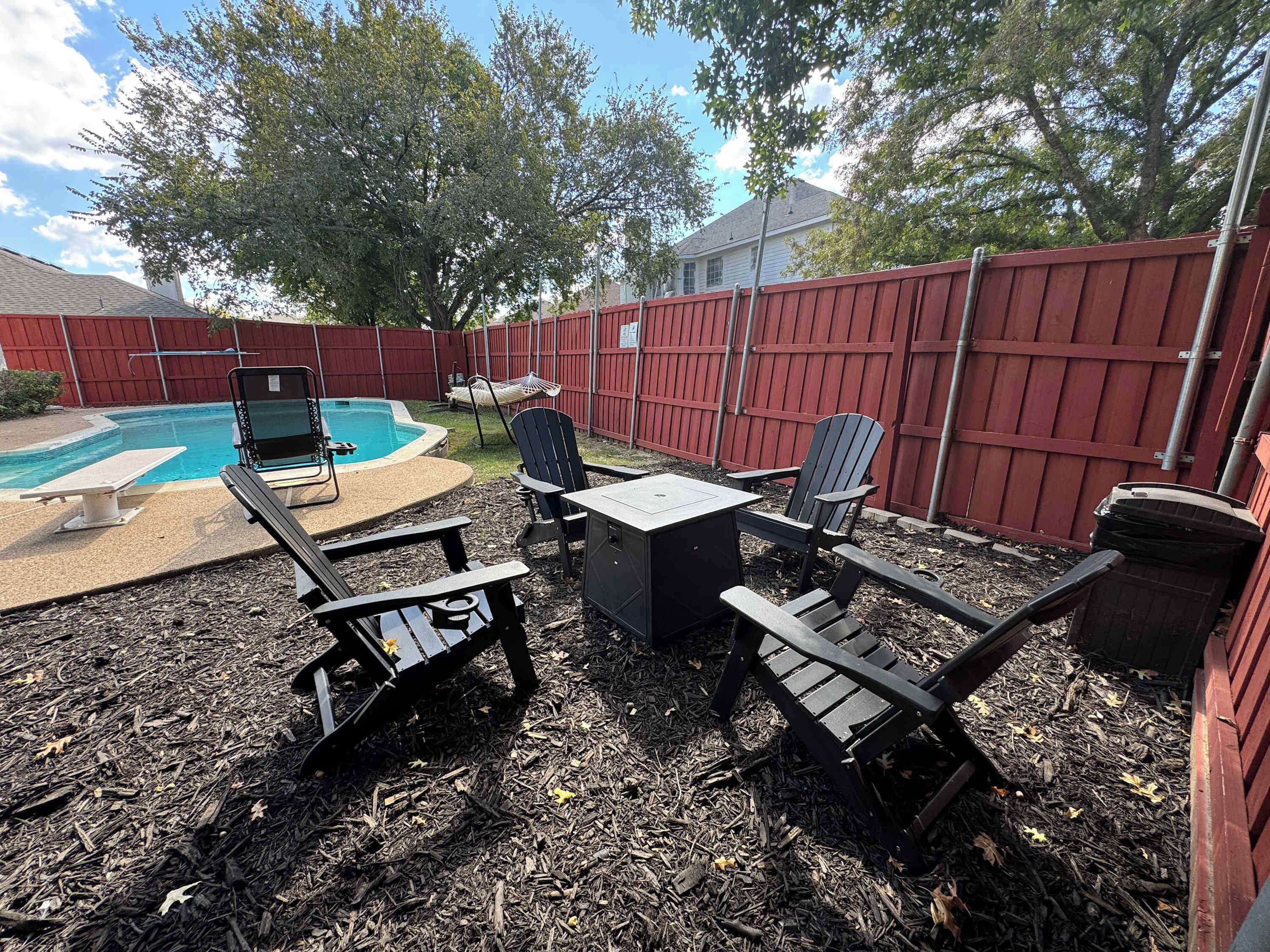 A backyard with a pool, outdoor furniture, and a red fence.