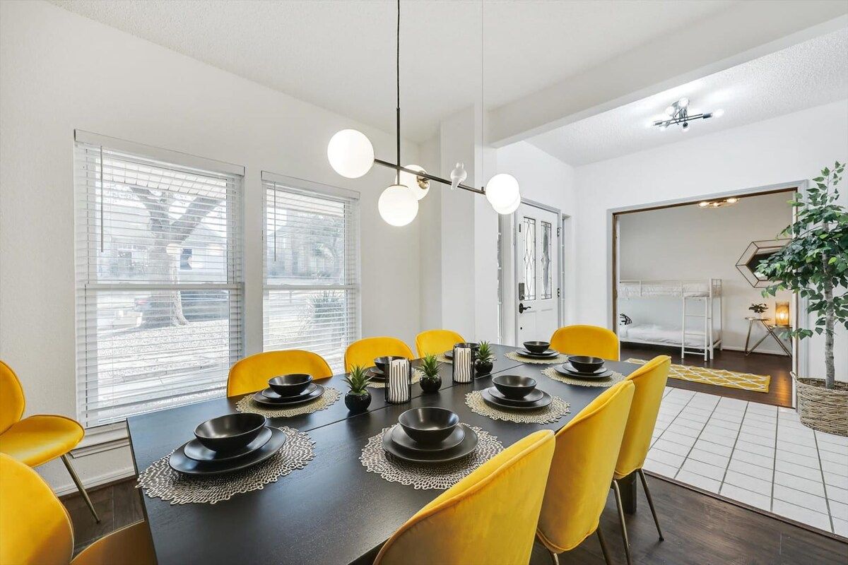 A dining area with a dark table, yellow chairs, and a modern chandelier.