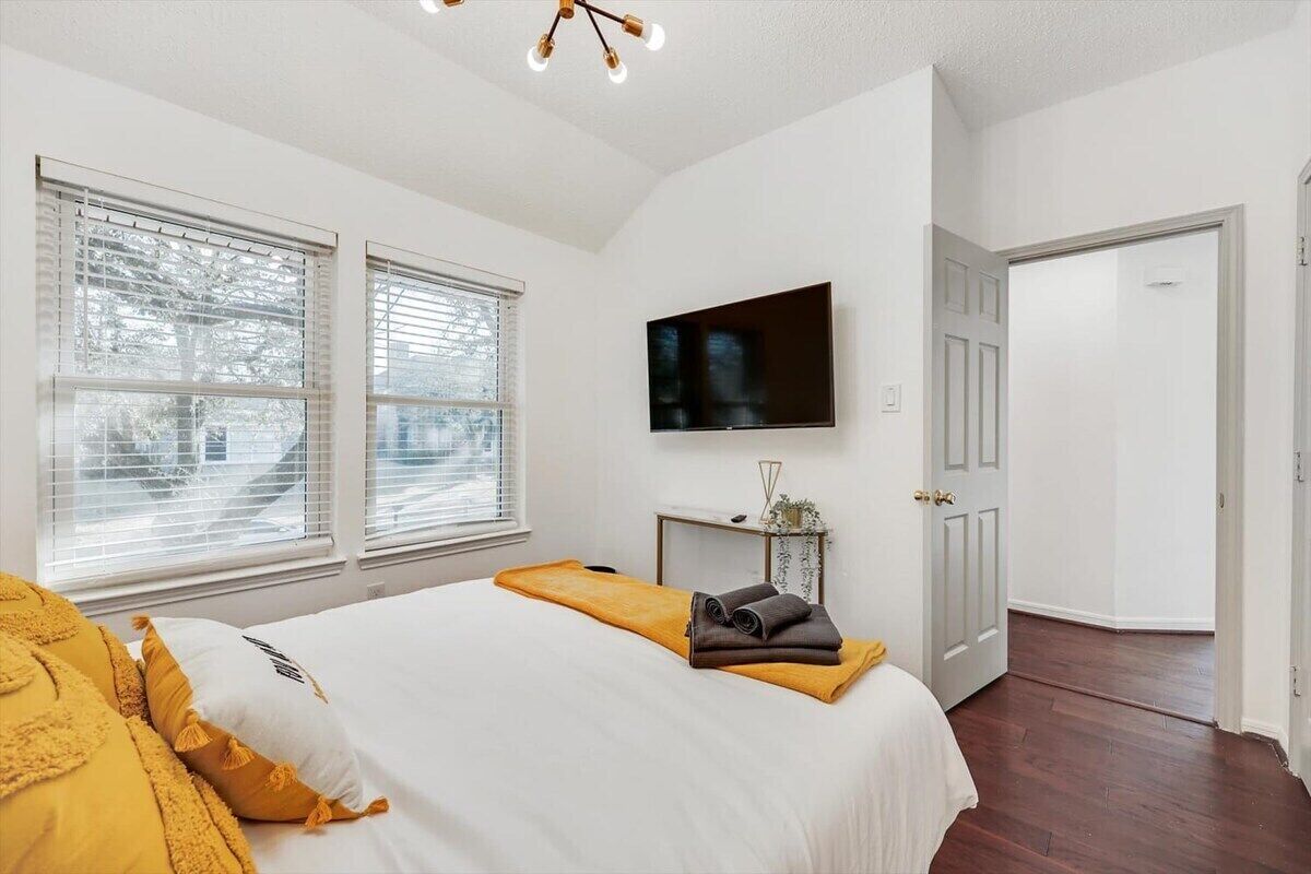 A bedroom with a bed, a TV, a door, and windows.