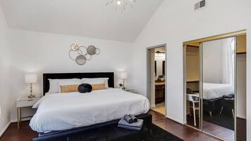 A modern hotel room with a large bed, a desk, a chair, a mirror, and a ceiling light fixture.