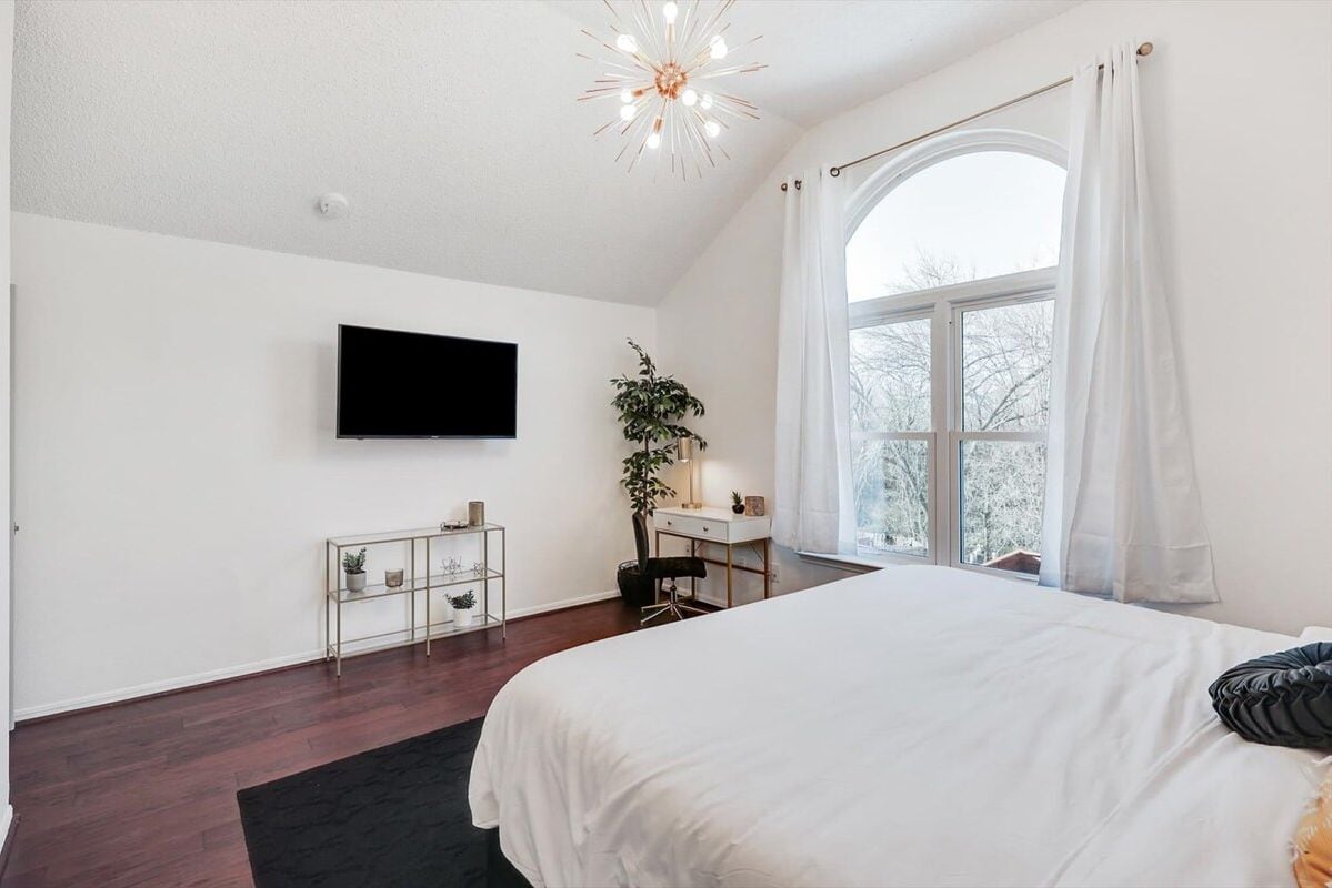 A bedroom with a large bed, a desk, a TV, and a window with curtains.