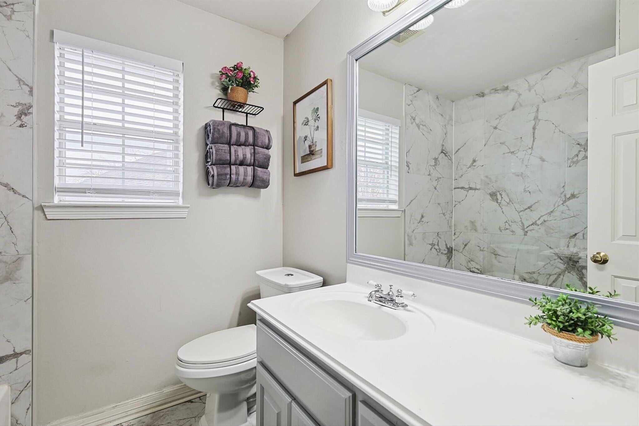 A bathroom with a white sink, a large mirror, a toilet, and a window with blinds.