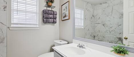 A bathroom with a white sink, a large mirror, a toilet, and a window with blinds.