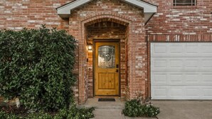 Une maison en briques avec une porte d’entrée en bois, une porte de garage et une haie bien entretenue.