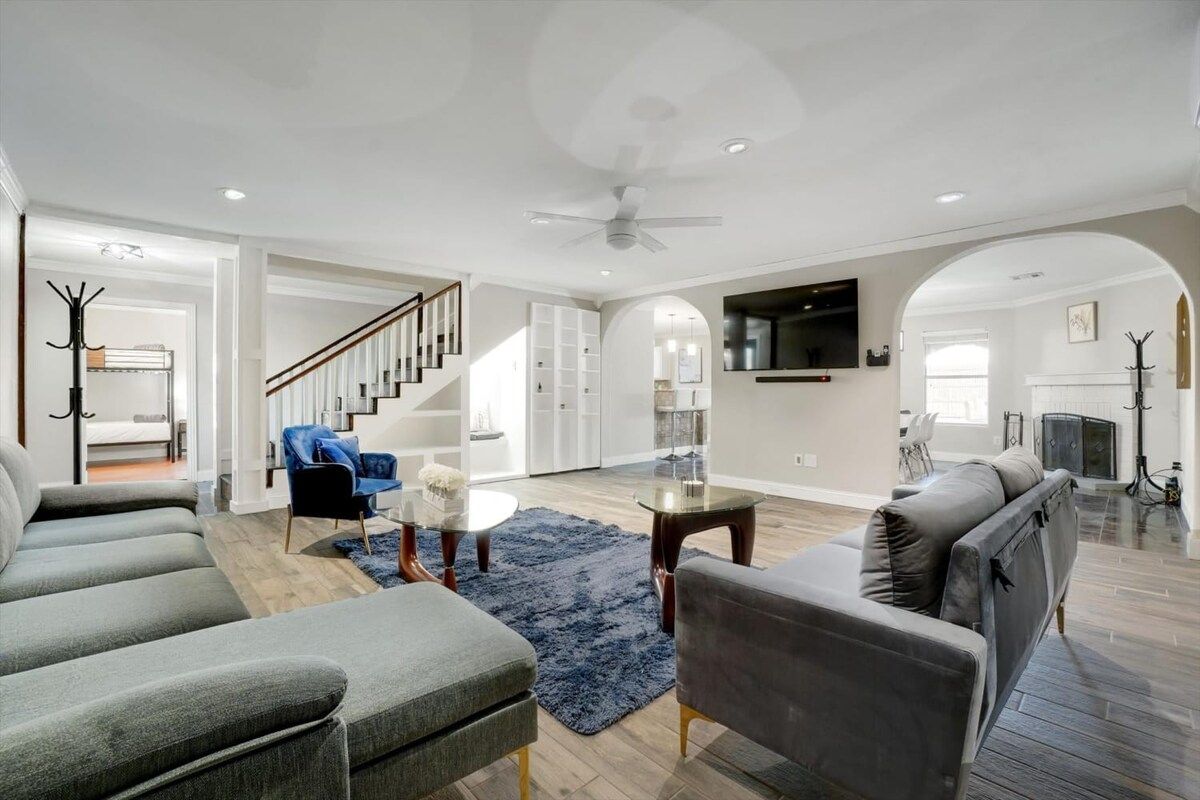 A spacious living room with a staircase, a flat-screen TV mounted on the wall, and a fireplace.