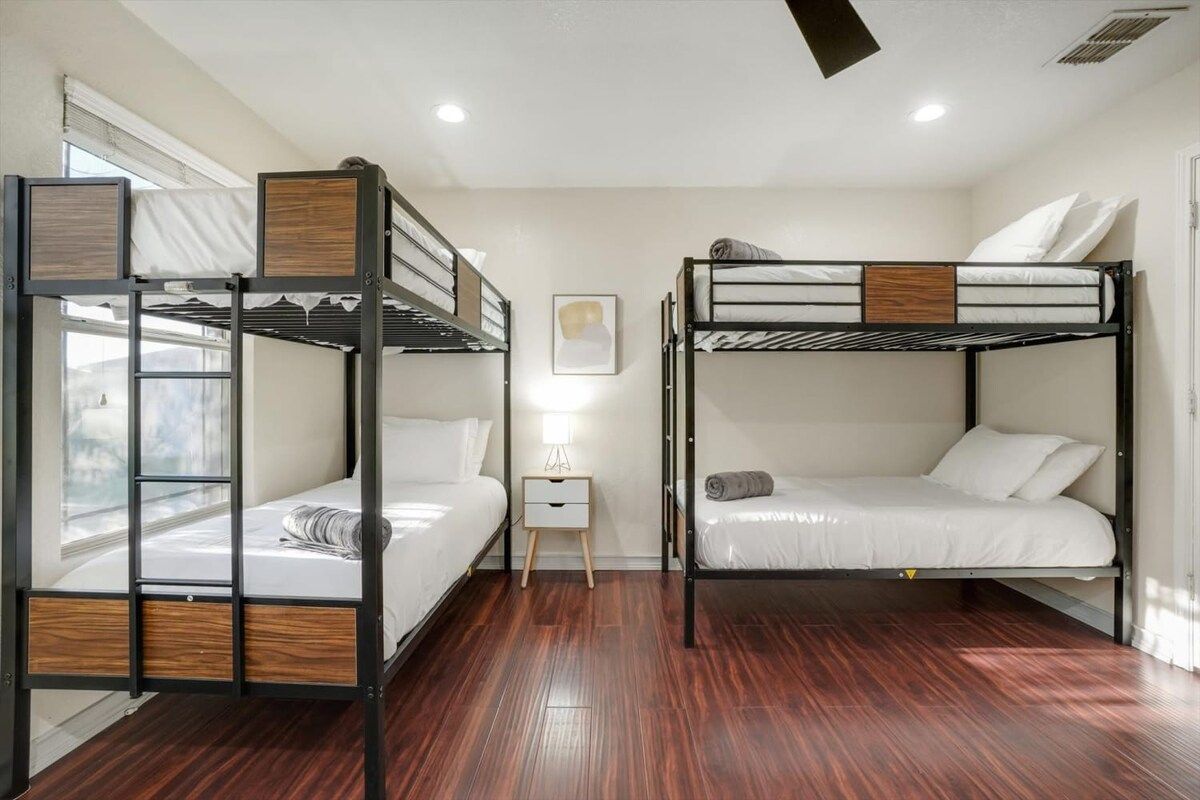 A room with two bunk beds, a small bedside table, a lamp, and a framed picture on the wall.
