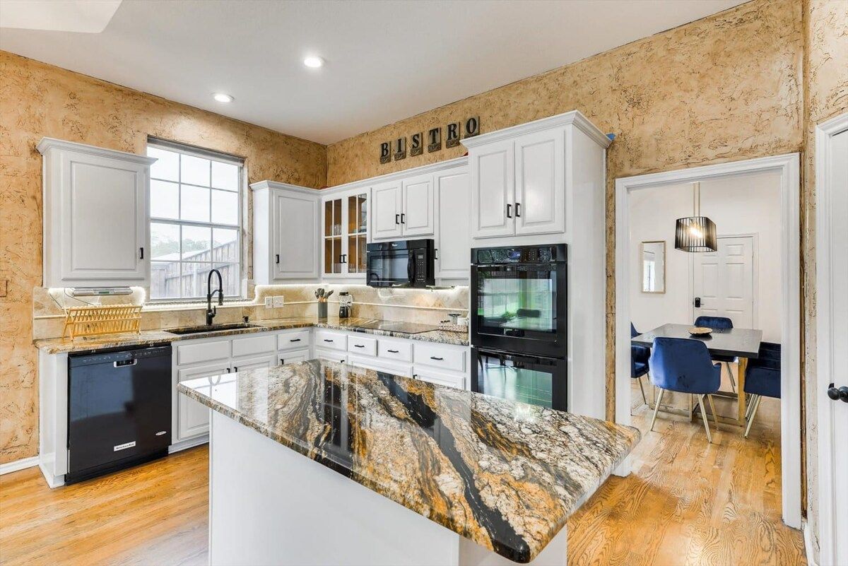 A modern kitchen with white cabinetry, a granite countertop, and a dining area with blue chairs.