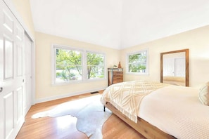Une chambre à coucher comprenant un lit, une commode et deux fenêtres donnant sur un paysage verdoyant.