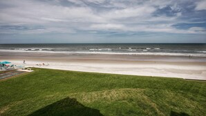 Une plage avec une zone herbeuse, une piscine et des chaises longues.