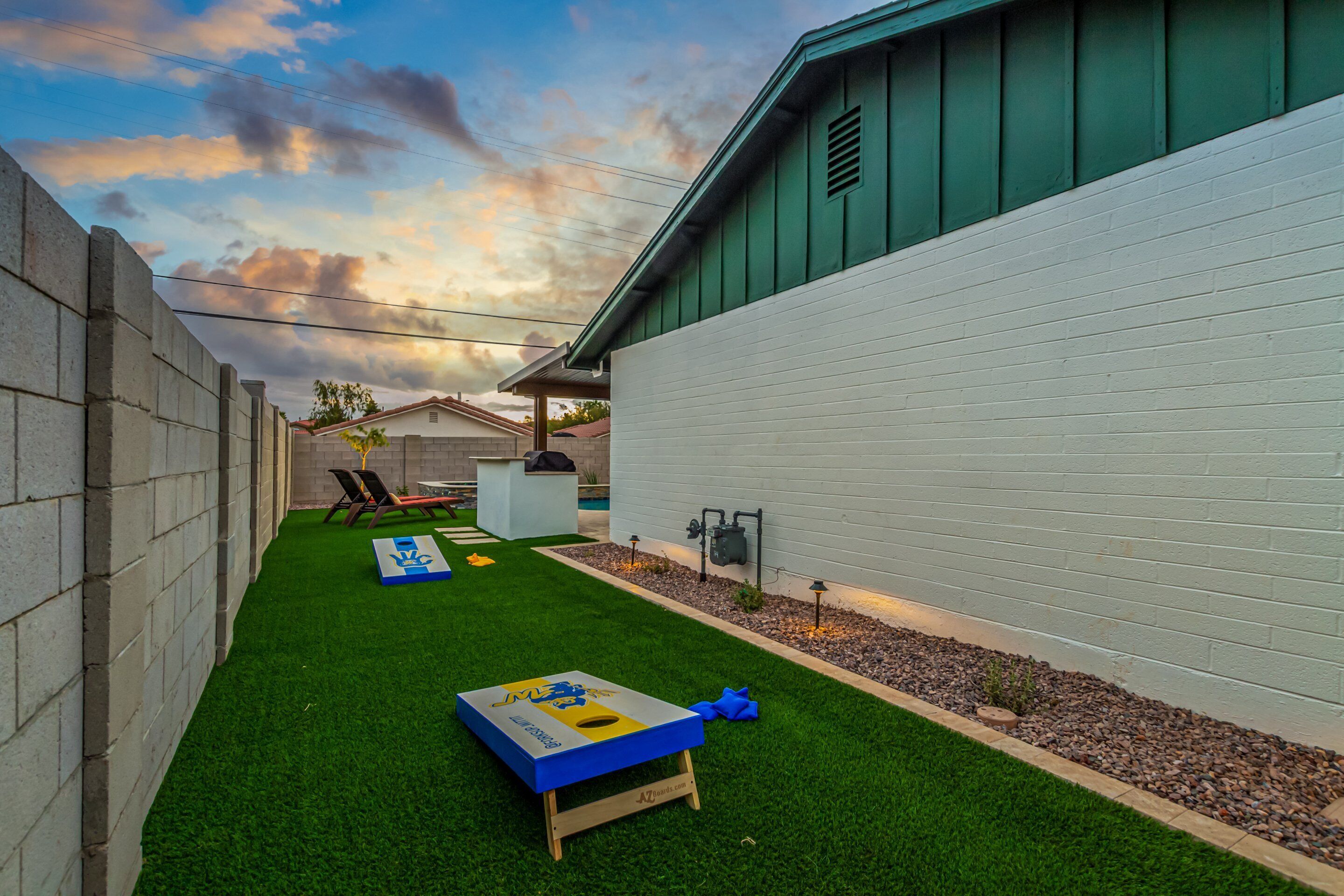 A backyard with artificial grass, a wooden play table, and a white wall.