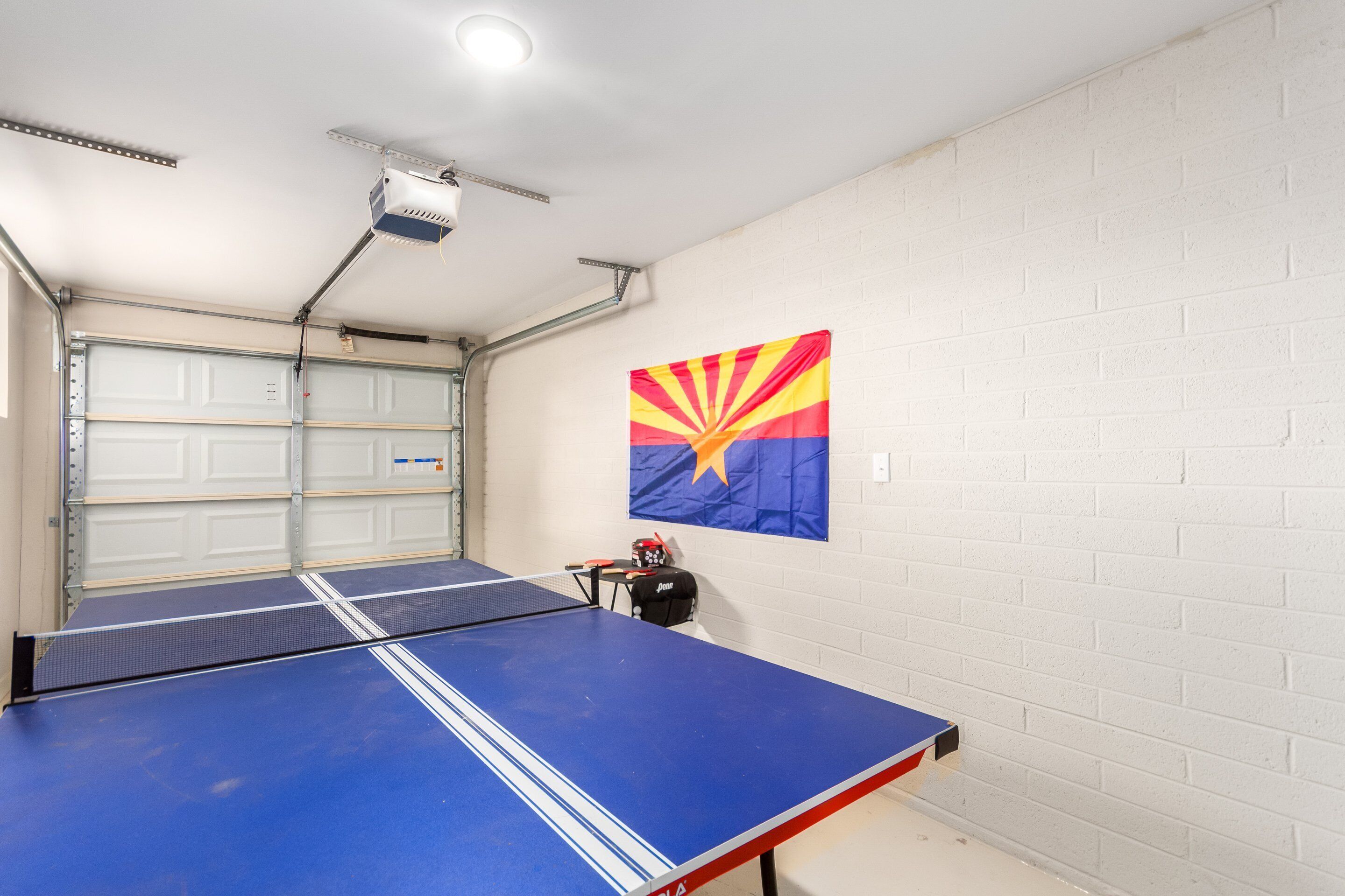 A ping pong table in a garage with a white brick wall and a flag.